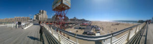 A panoramic picture of an elevated boardwalk, large hotels and a beach stretching into the distance.