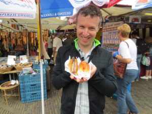 A man holding two buns with fish in them in front of a market stall.